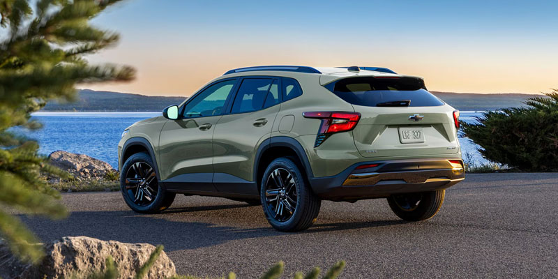 A sage green Chevrolet Trax parked on a paved overlook with a scenic lake and mountains in the background.
