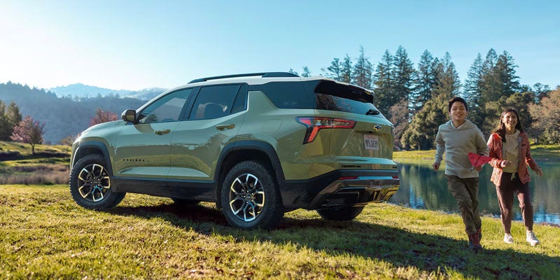 Two children running around the back of a Chevy Equinox parked in a field of grass